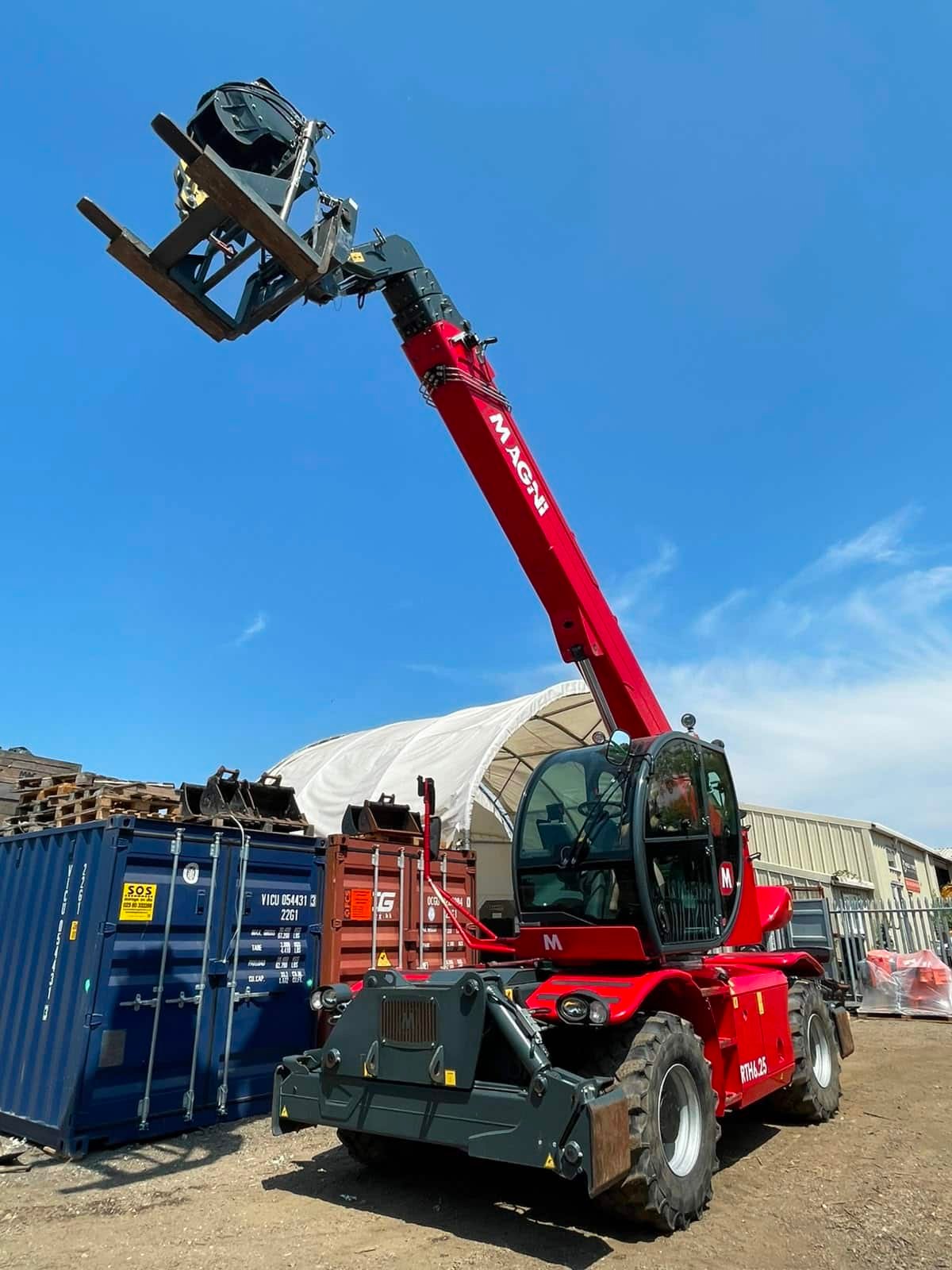 Red telehandler lifting forks beside shipping containers