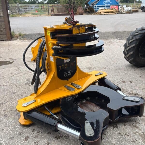 Yellow hydraulic tree shear attachment on farmyard