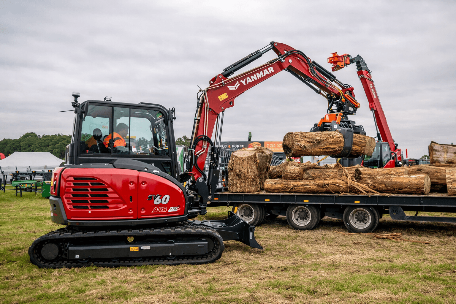 Red mini excavator loading logs onto trailer