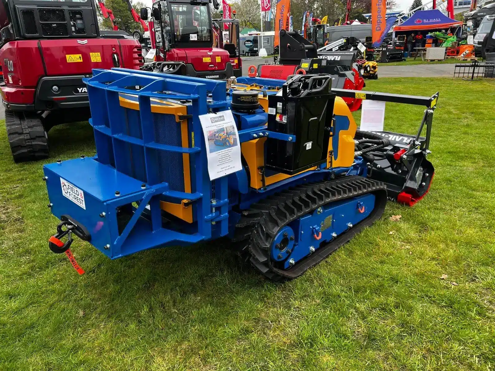 Bomford Flailbot remote‑controlled tracked mower with custom-fitted reinforced rear guard displayed at outdoor machinery show.